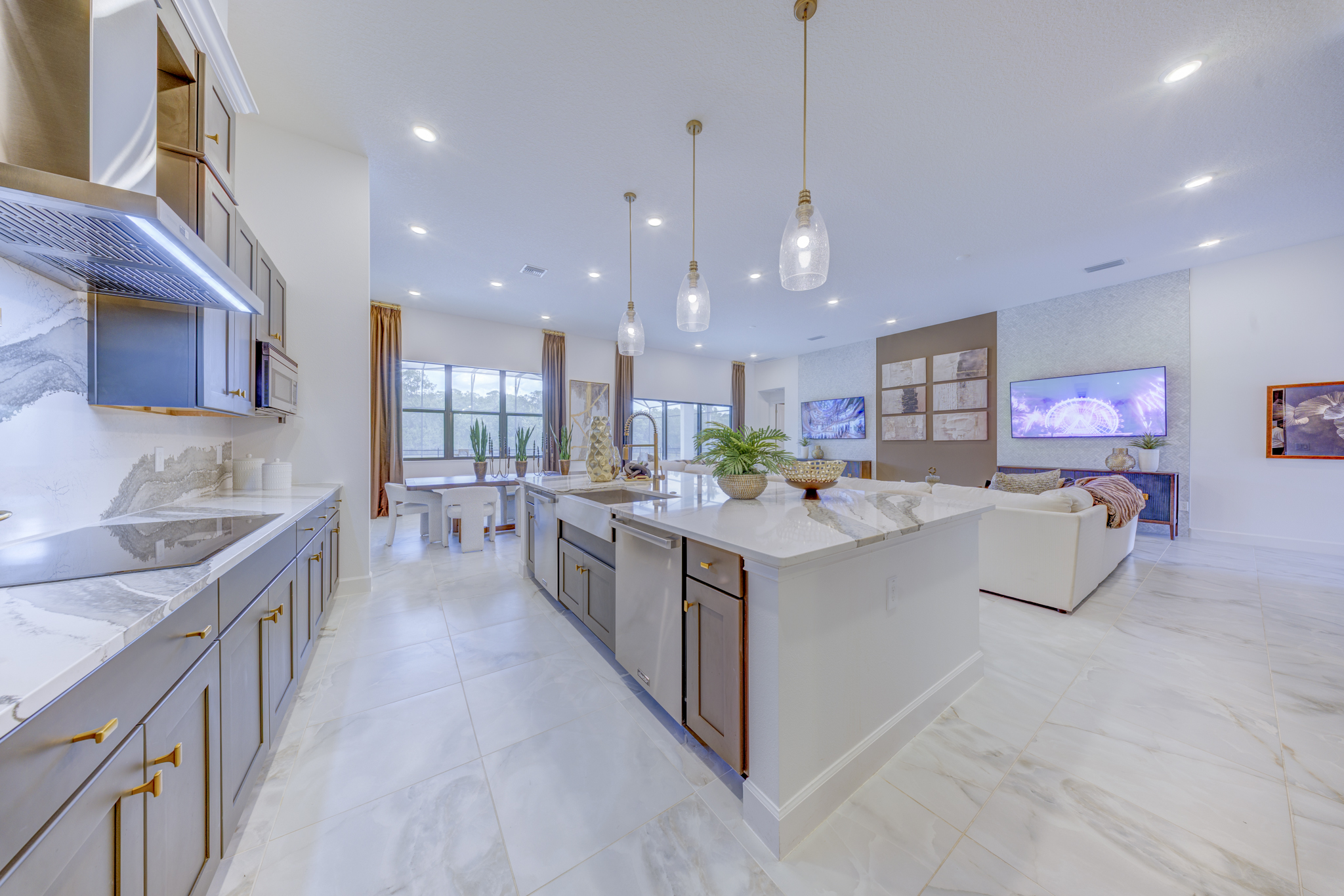 Wide kitchen view with large marble island, undermount sink, gold fixtures and open view to living room and pool