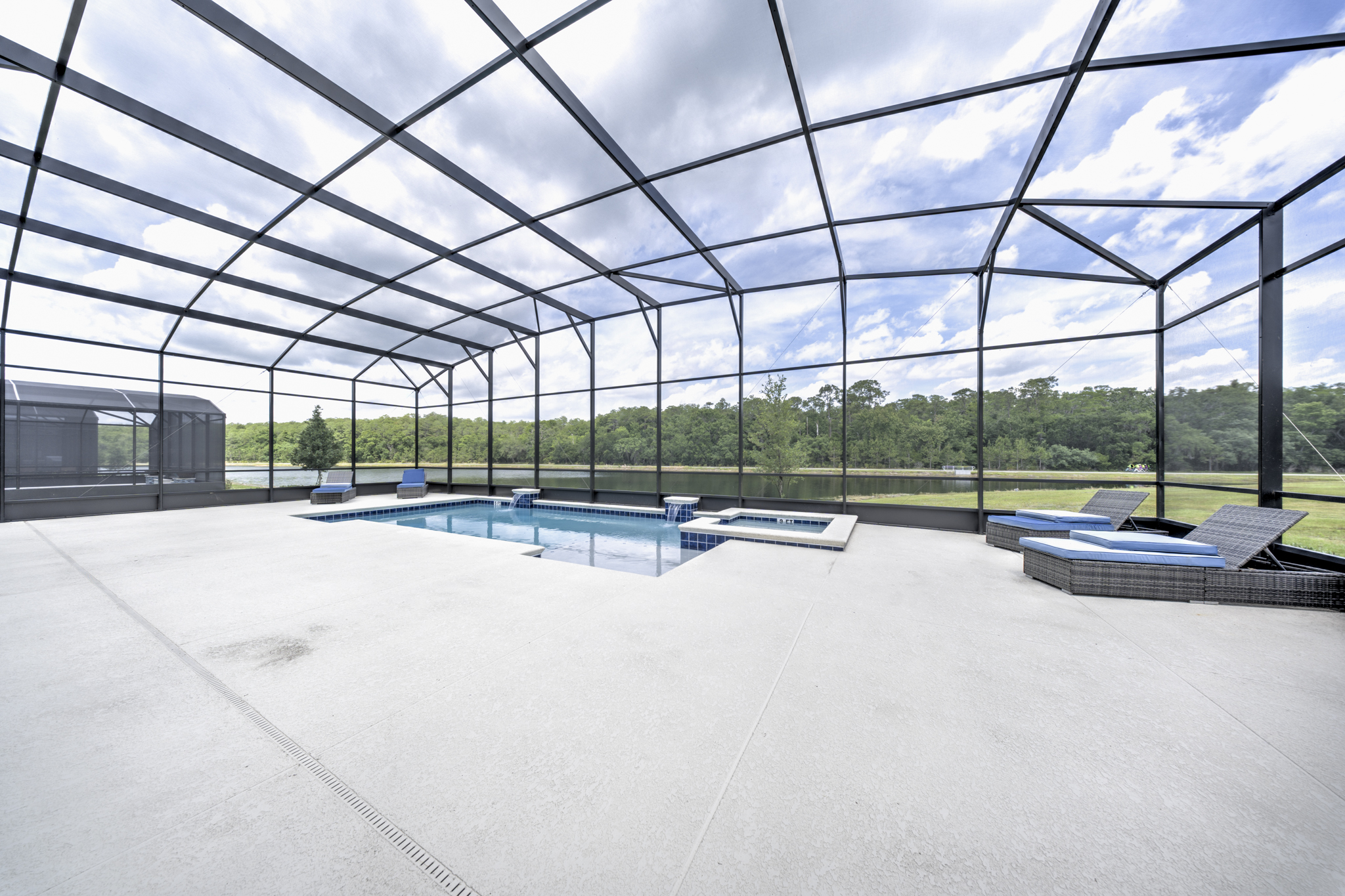 Screened pool enclosure with rectangular pool, attached spa with water feature and lounge chairs overlooking lake