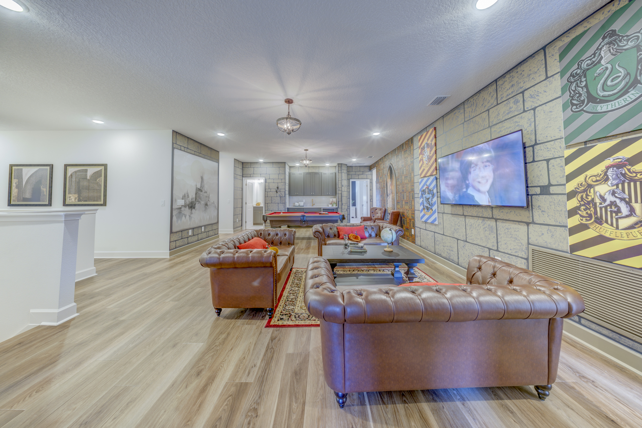 Harry Potter-themed game room with Chesterfield leather sofas, pool table, stone wall mural and house crests