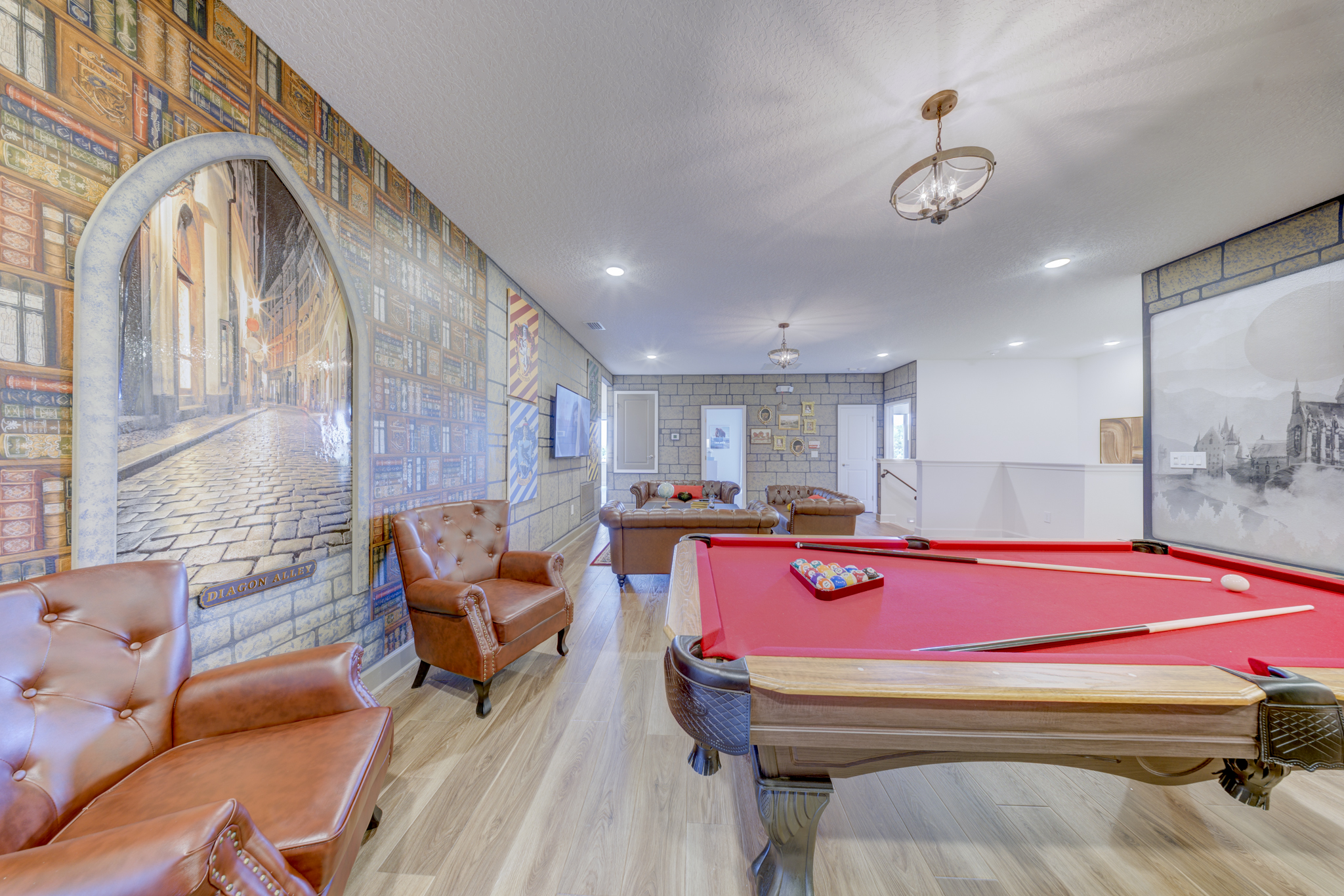 Game room with Diagon Alley bookshop mural, pool table with red felt, leather armchairs and chandelier