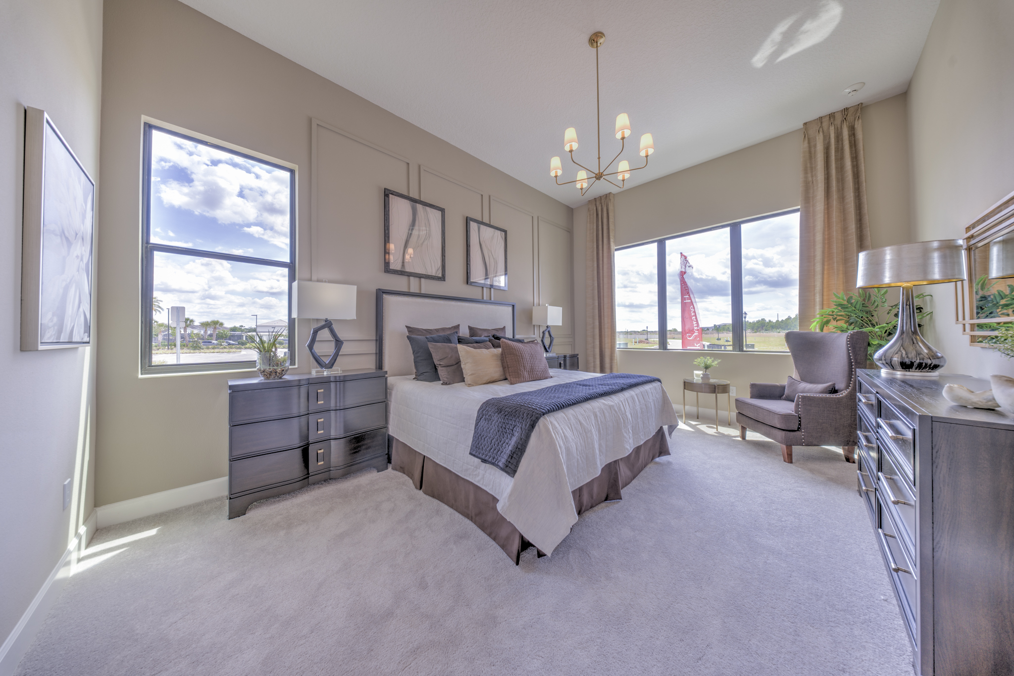 Primary bedroom with vaulted ceiling, gold chandelier, upholstered gray king headboard and large windows