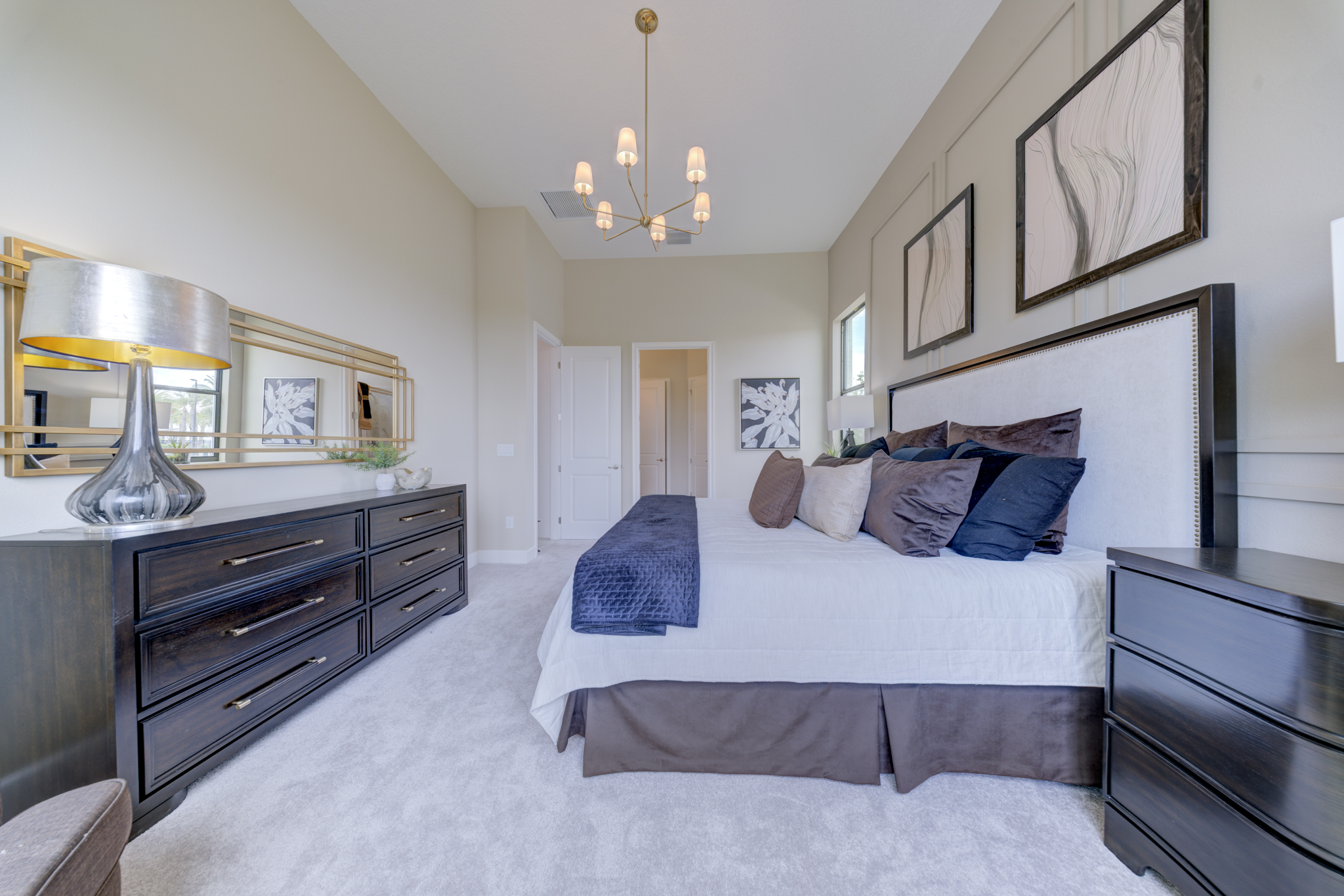 Primary bedroom alternate view with vaulted ceiling, chandelier and dark wood dresser with mirror