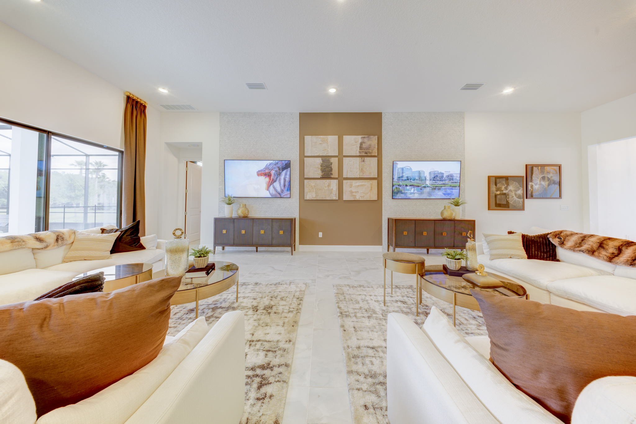 Great room with two facing white sofas, dual entertainment consoles, brown accent wall with gallery art and wall-mounted TVs