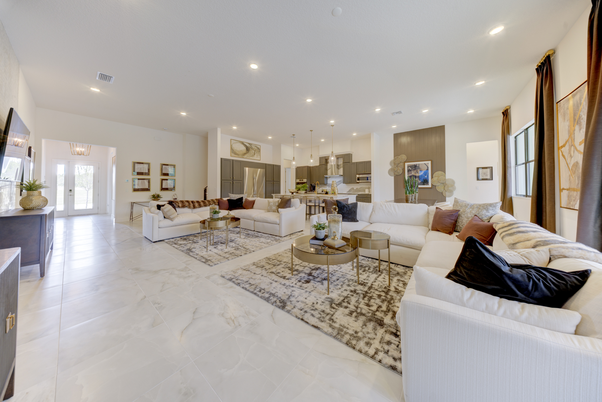 Expansive great room with two white sectional sofas, gold-accent coffee tables and kitchen beyond